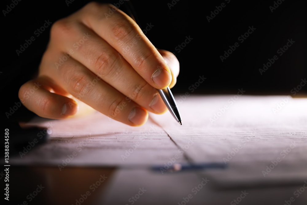 Close-Up of Hand Writing with Pen on Document in Dark Room