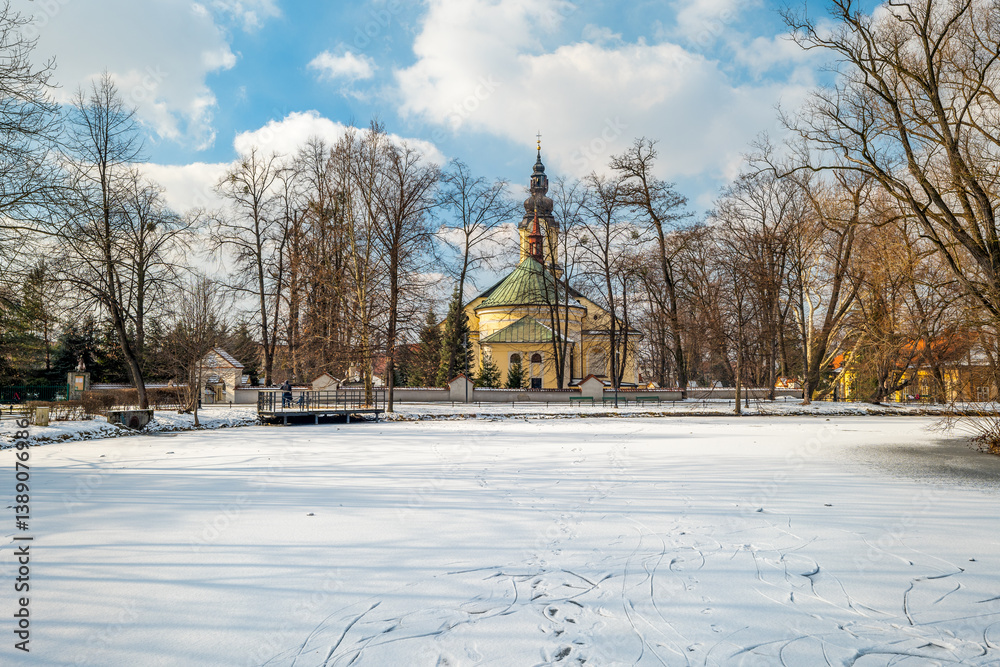 View of the frozen, snow-covered Pond in the City Park in Andrychów. Church in the background. Lesser Poland Voivodeship