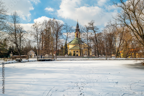Obraz na płótnie View of the frozen, snow-covered Pond in the City Park in Andrychów. Church in the background. Lesser Poland Voivodeship w salonie
