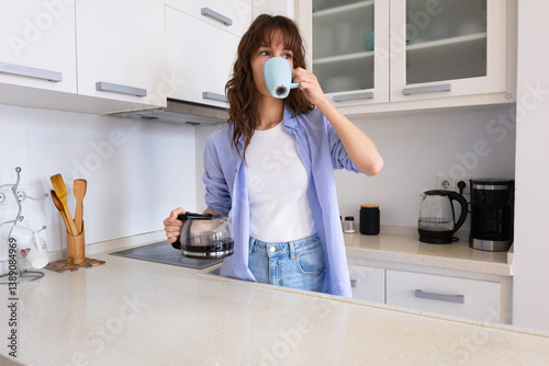 Beautiful curly brunette with the cup drinking coffee in the kitchen at home in the morning