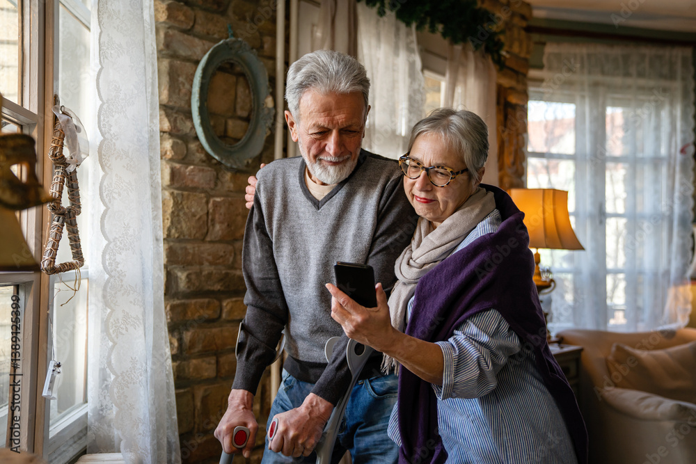 Senior wife embracing disabled husband at nursing home. Cheerful old couple using mobile phone.