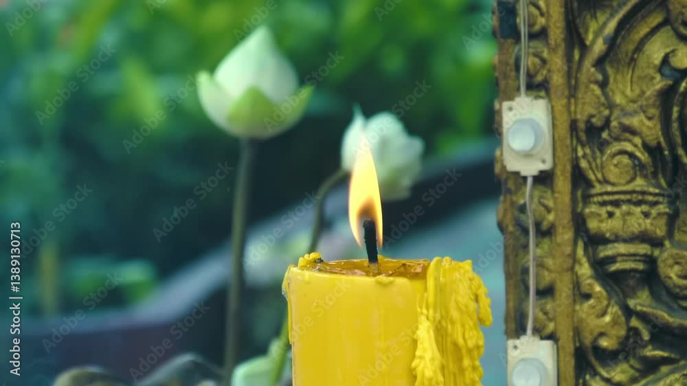 A big yellow wax candle is burning as a light offering in the temple as well as lotus flowers, Cambodia. Closeup. Slow motion