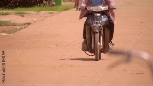 A man rides an old motorcycle along a rural dirt road and a woman takes her children to school, Cambodia. Closeup. Slow mo, slow motion, high speed camera, 200 fps