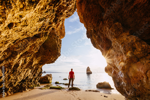 Man enjoying sunrise on the beach from a cave, Algarve, Portugal