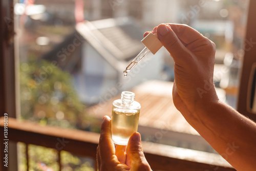 Female hands holding a glass bottle of hair and skin care oil against the sun's rays. Glass pipette with a drop of moisturizing face serum with oils