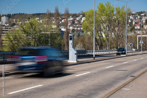 Blurry cares driving by a gray, mobile, car traffic speed trap camera between two car lane. Close up, telephoto shot