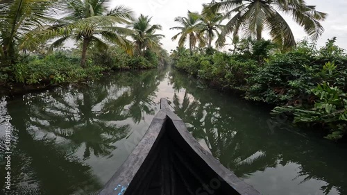 Wooden boat ride in the tropical canals of Varkala, India. Calm water reflects lush trees, capturing a peaceful and authentic moment in nature.