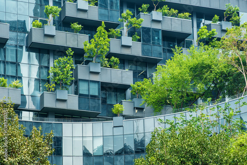 Building facade with green plants growth on the wall. Vertical garden in Bangkok city. Eco friendly urban environment. Sustainable modern and ecological architecture.Sustainable glass office building