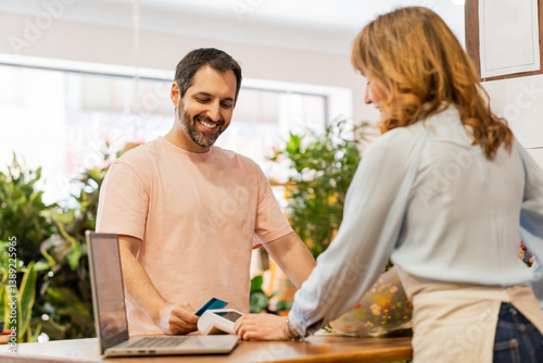 Florist accepting contactless payment from customer in flower shop