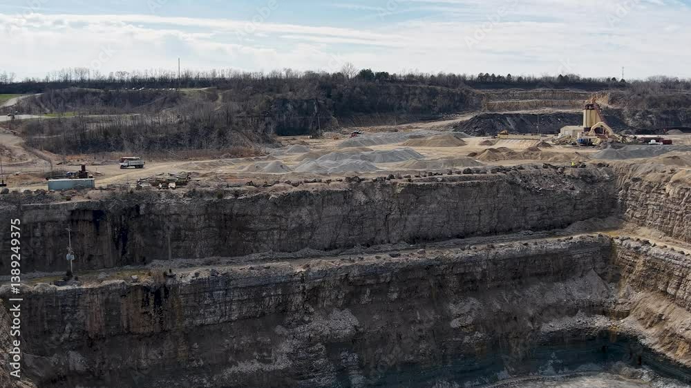 High-altitude view of a multilevel open-pit excavation site with dramatic terraced stone walls and exposed geological layers under overcast skies High-altitude view of a multilevel open-pit excavation site with dramatic terraced stone walls and exposed geological layers under overcast skies
