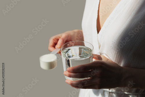 Woman hands with a scoop with collagen or protein powder and a glass of water. Trendy beauty supplement for healthy skin and bones.