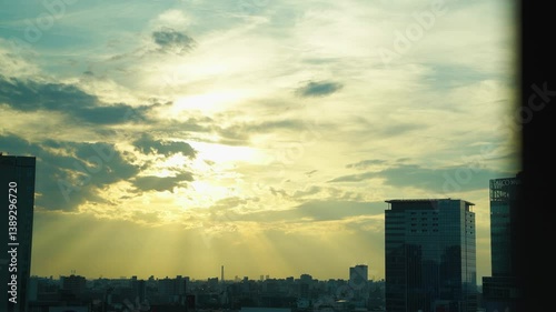 Sky and sunlight break through clouds amid silhouette buildings in Tokyo.