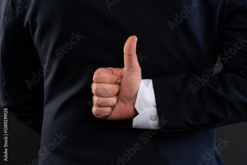 Close-up of hidden thumbs up behind business suit.