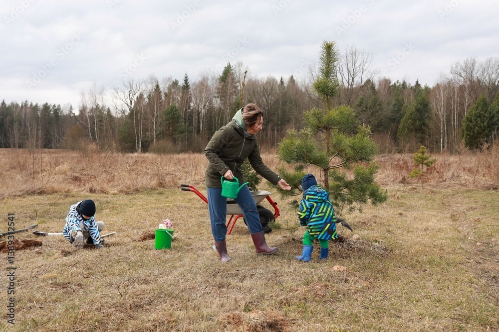 Family planting trees in a grassy area surrounded by forest in early spring
