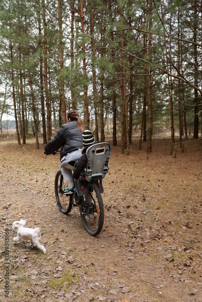 Family bicycle ride through a wooded trail with a child and a small dog during a cloudy day
