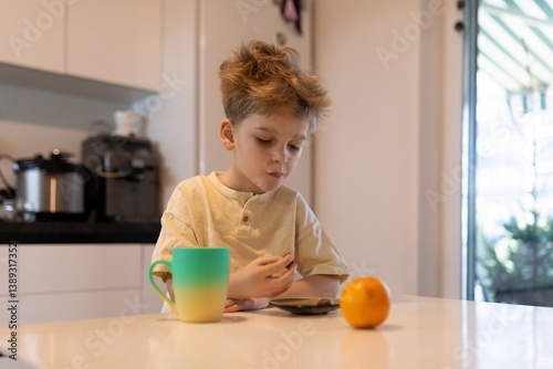 Obraz na płótnie Child enjoying breakfast with orange and beverage while using a tablet in a modern kitchen setting w salonie