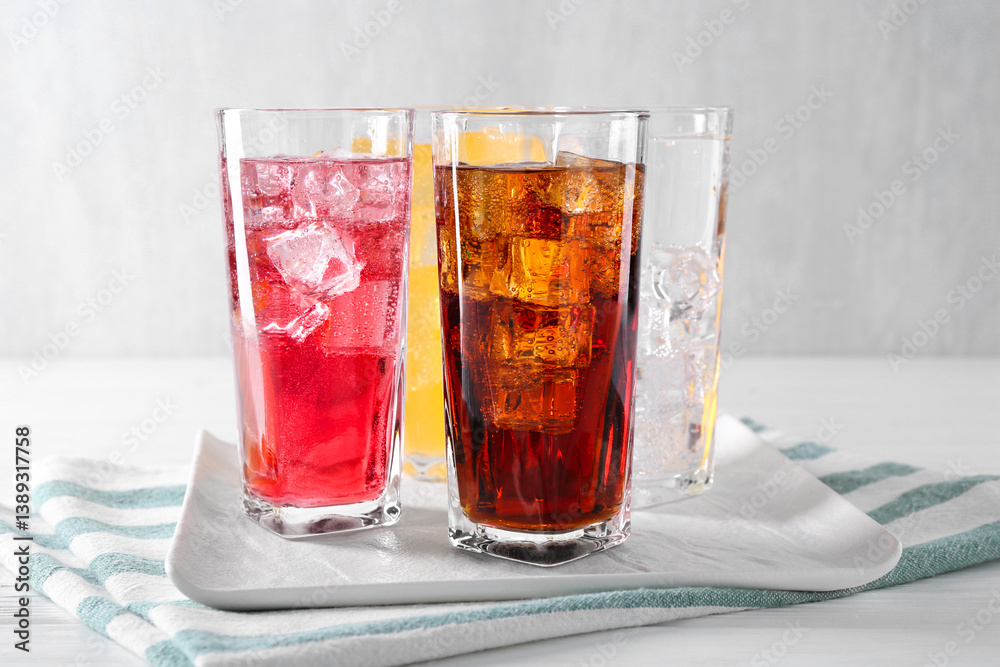 Soda water of different flavors with ice cubes in glasses on white wooden table