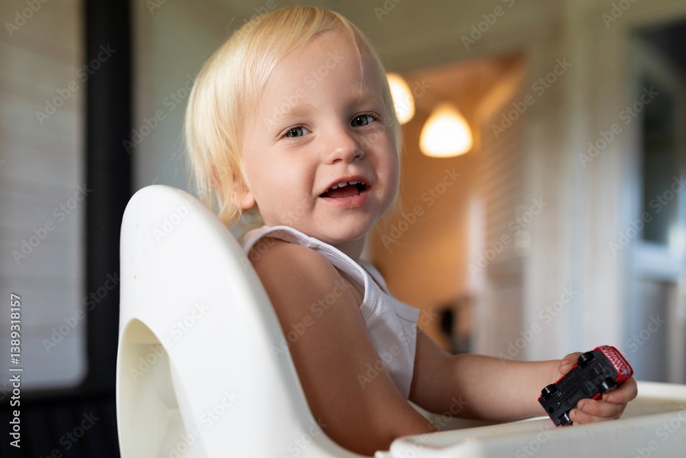Happy toddler playing with toy truck in high chair during a sunny afternoon at home