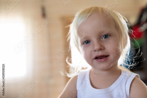 Child with light blonde hair smiling in a cozy indoor setting during daylight hours, capturing innocence and joy of childhood