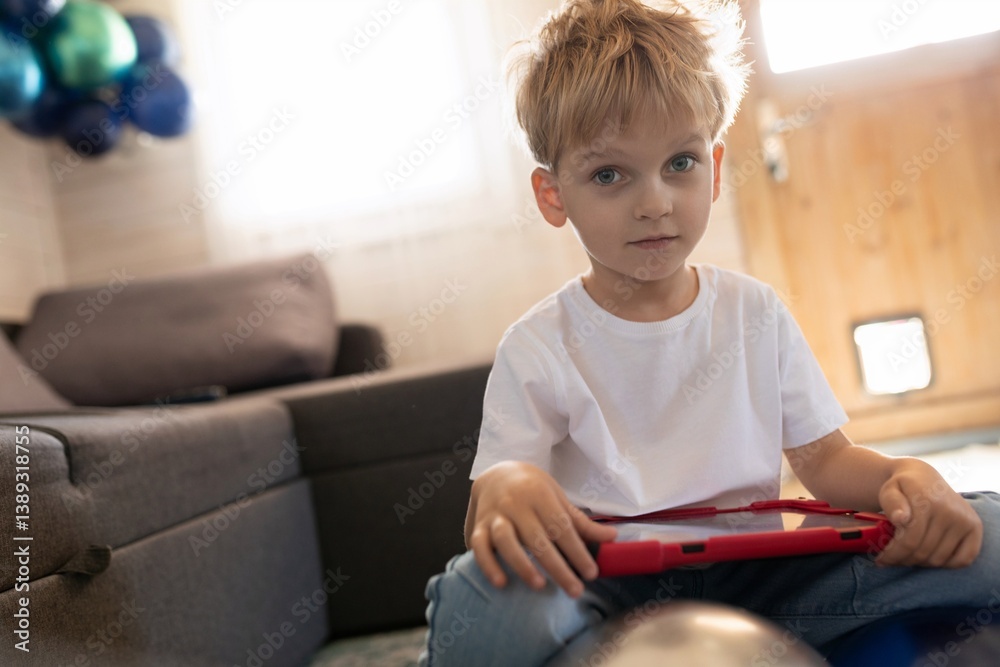 Young boy playing with tablet in cozy living room during daytime surrounded by festive decorations