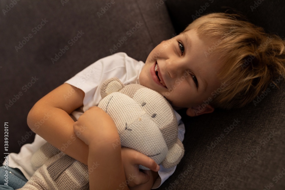 Smiling boy cuddling a stuffed animal on a couch during a cozy afternoon at home