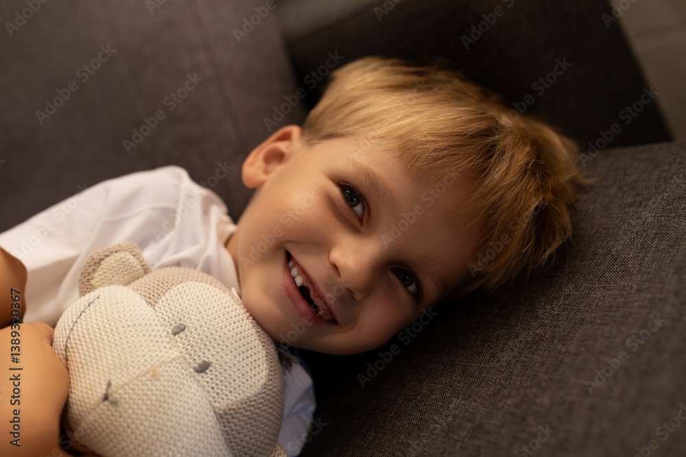 Smiling child resting on couch with stuffed animal in cozy indoor setting