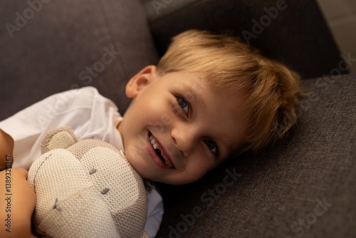 Obraz na płótnie Smiling child resting on couch with stuffed animal in cozy indoor setting w salonie