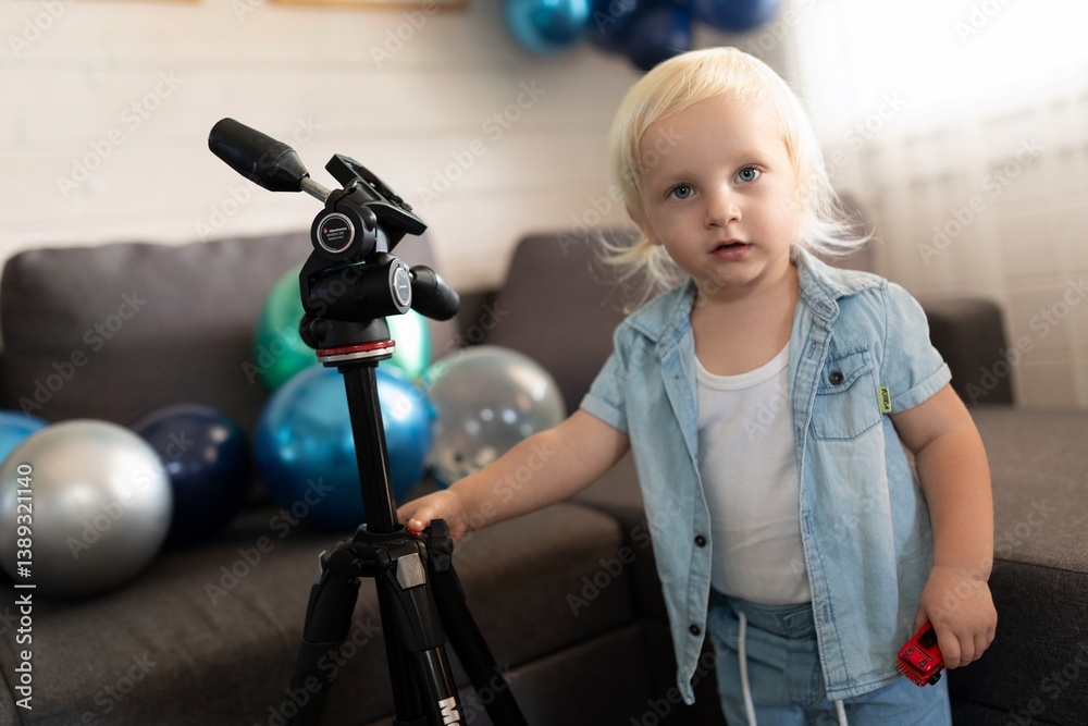 Child explores a tripod in a colorful indoor setting filled with balloons during a festive celebration