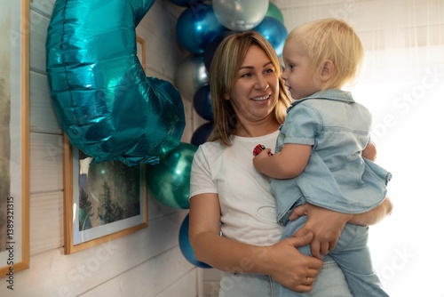 Celebration moment with a joyful mother holding her baby in a decorated indoor space filled with balloons