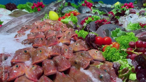 Pile of red gurnard fish heads on crushed ice with cherry tomatoes and greens in fishery stall market
