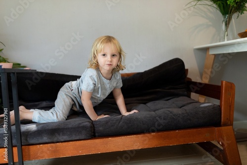 Child playing on a cozy bed in a bright living room during the afternoon sunlight