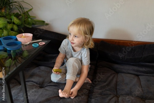 Child enjoying snack on cozy couch in a bright room with indoor plants while seated at glass table