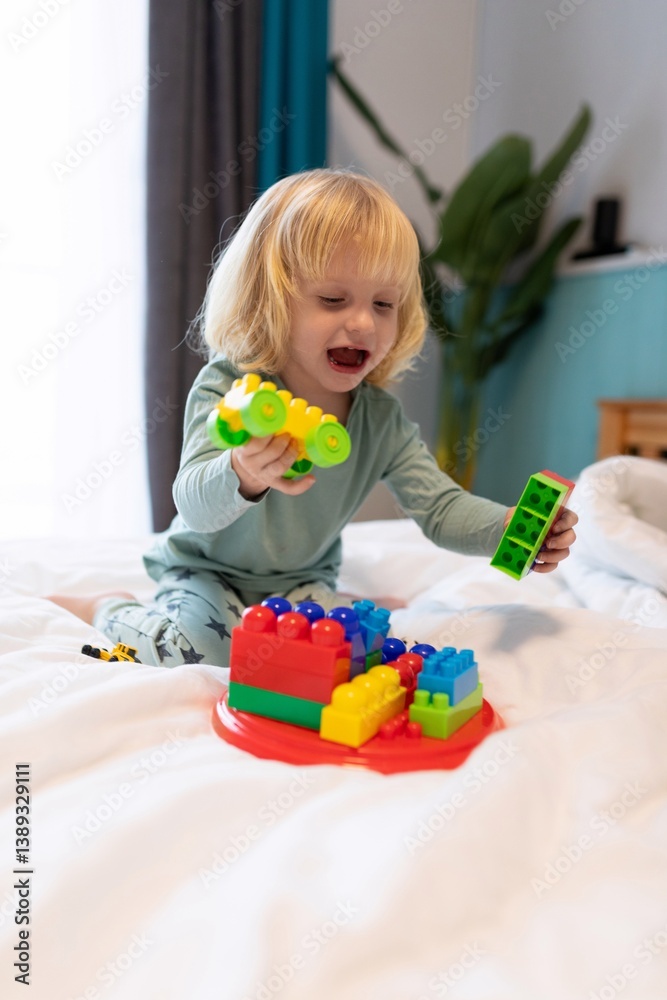 Child joyfully builds with colorful toy blocks on a bed in a bright indoor space during the day