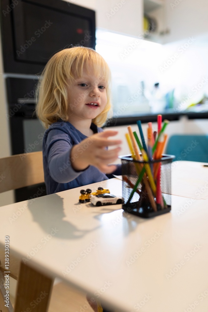 Young child interacts with colorful craft materials at a modern kitchen table during a creative activity
