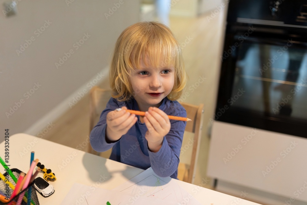 Young child enjoys creative time with colored pencils at a modern kitchen table in a cozy home setting