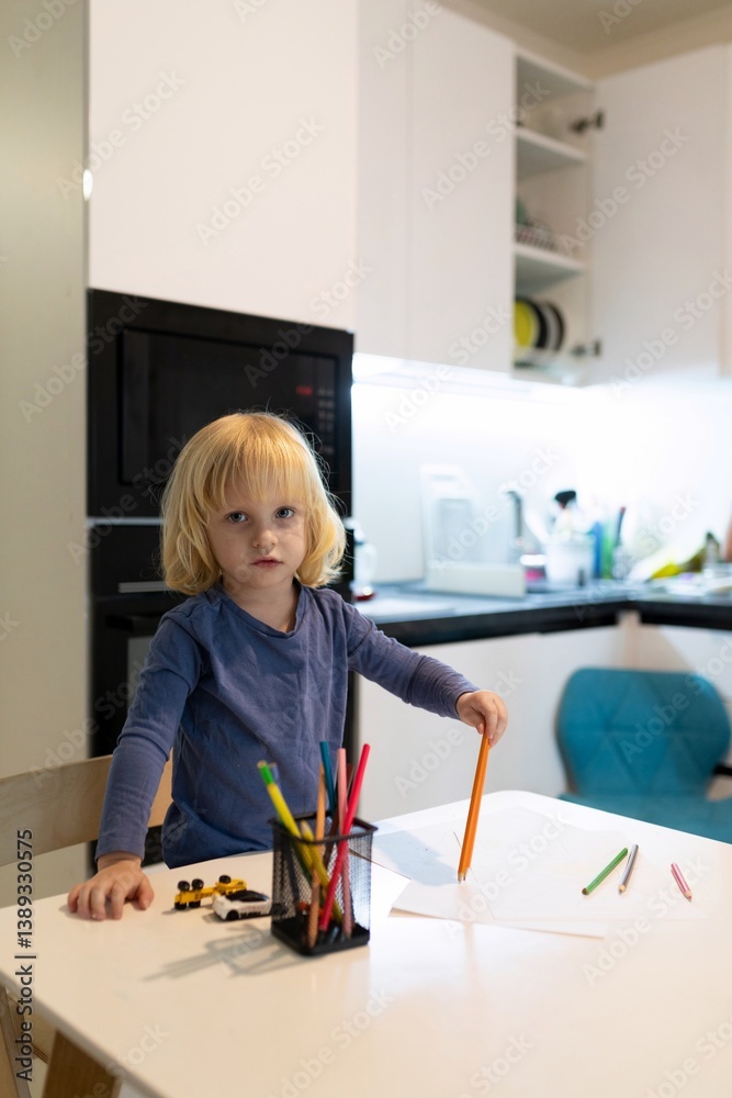 Child engaging in creative drawing with colored pencils in a modern kitchen setting during the afternoon