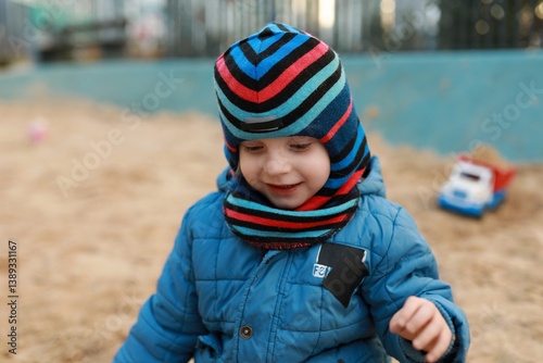 Obraz na płótnie Child enjoying playtime in a sandbox at a park during a cool autumn afternoon while wearing a colorful hat and scarf w salonie