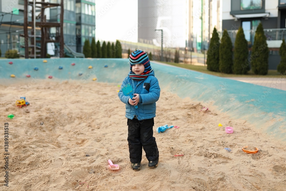 Child playing in a sandy area with toys on a sunny day in an urban environment