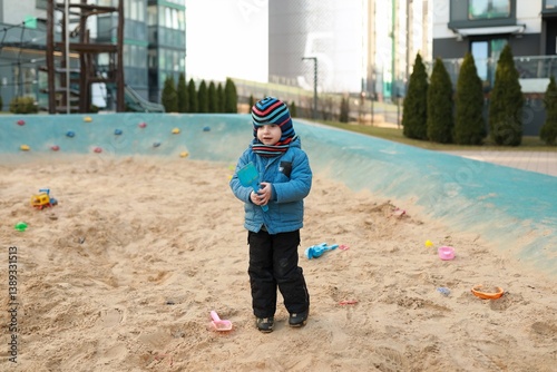 Obraz na płótnie Child playing in a sandy area with toys on a sunny day in an urban environment w salonie