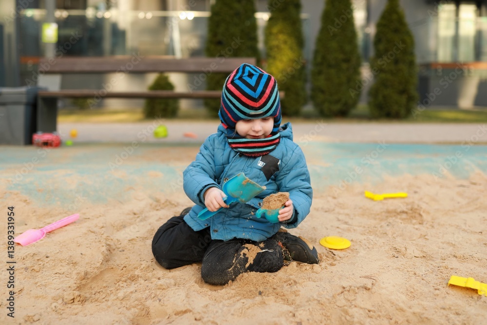 Child plays happily in sandbox using colorful toys in urban playground during sunny day