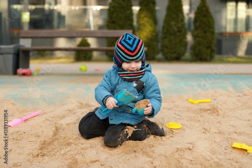 Child plays happily in sandbox using colorful toys in urban playground during sunny day