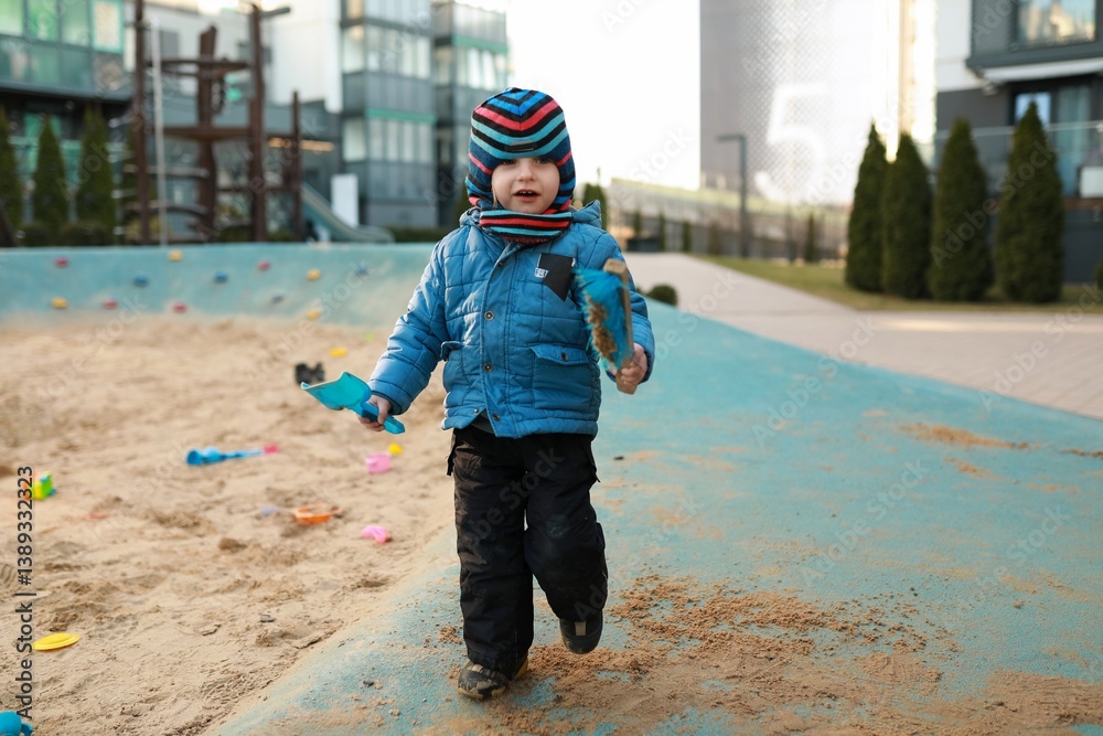 Young child enjoys playtime in a sandy area at a modern playground during the day