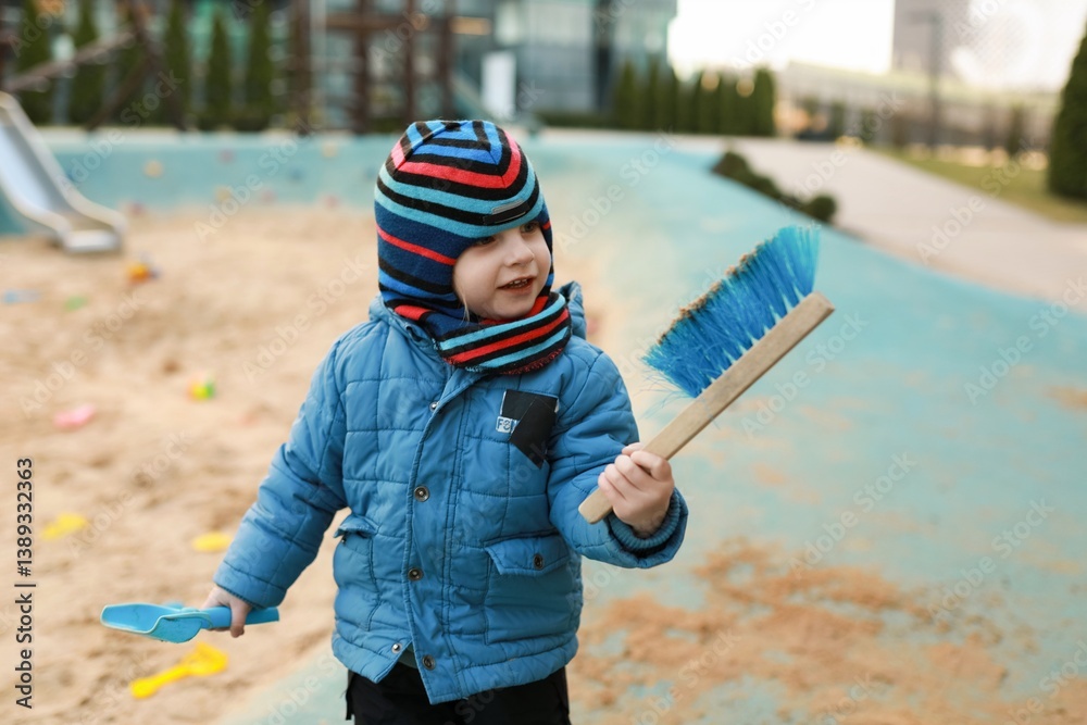 Child enjoying outdoor playtime in sandpit with colorful brush while wearing winter clothing