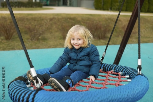 Obraz na płótnie Child enjoying a swing in a park during a sunny afternoon while wearing a warm jacket and smiling brightly w salonie