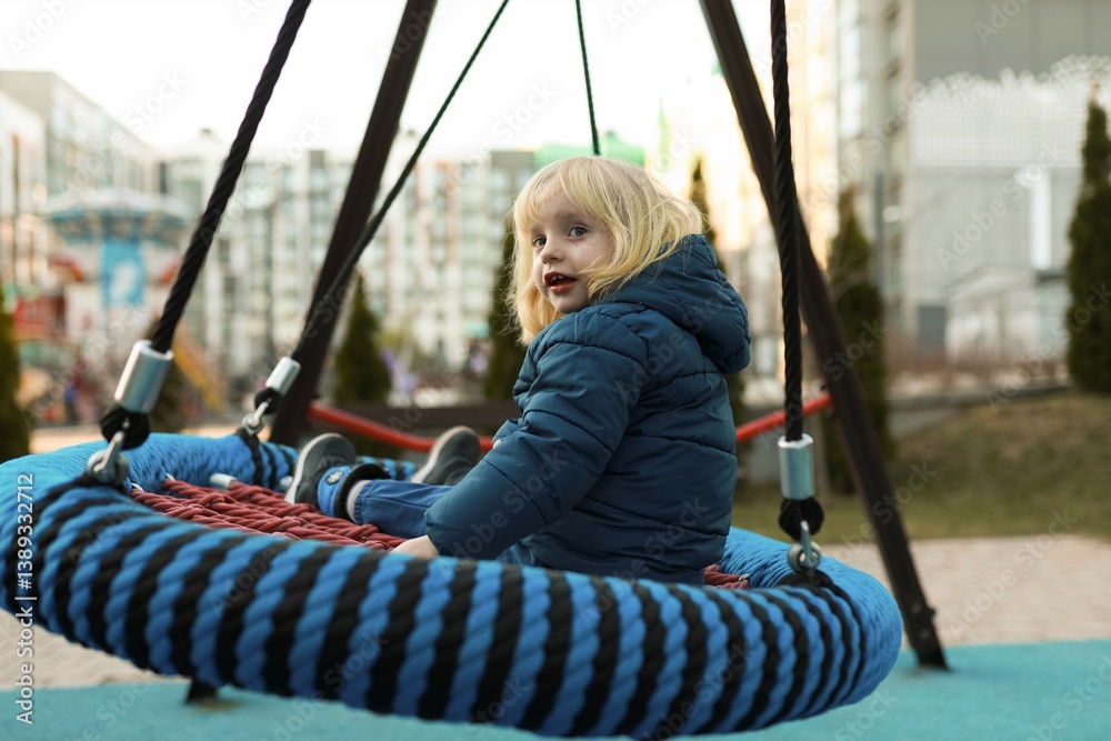 Child enjoys swinging on a large round swing in an urban park during the late afternoon hours