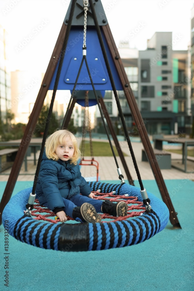 Child enjoying a swing on a playground in an urban park during the afternoon