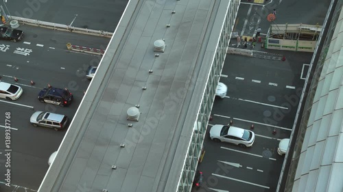 Shibuya traffic, low angle shot from a tall building showing cars driving under the overpass connecting the buildings on evening 