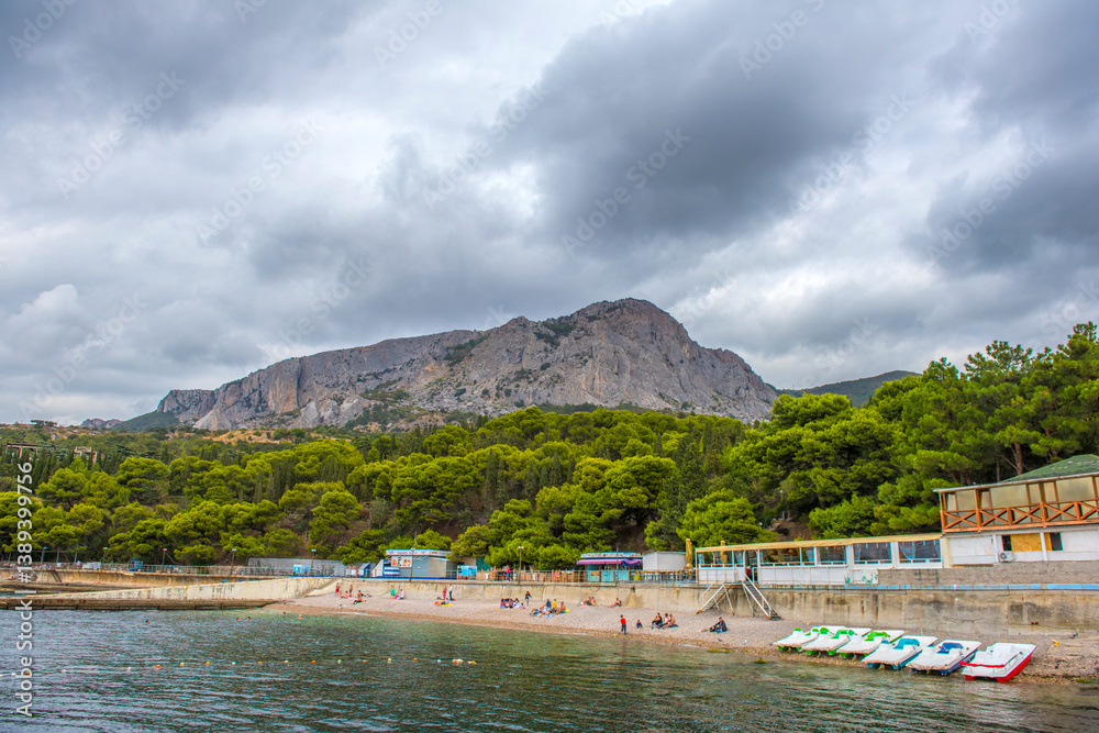 Fototapeta premium picturesque beach in Foros, Crimea. In the foreground is calm sea water with buoys, pebbles and a row of catamarans. 