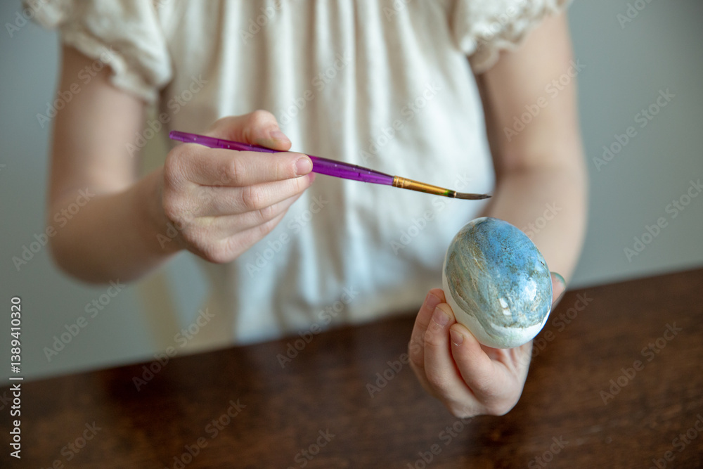 Close-up of a child's hand holding a paintbrush and an easter egg