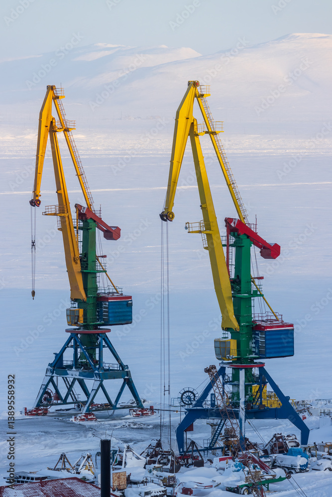 Cargo seaport in the Arctic. Large harbor cranes on a background of ice and snow. Winter industrial landscape. Industry and transport infrastructure in the Far North. Anadyr sea port, Chukotka, Russia